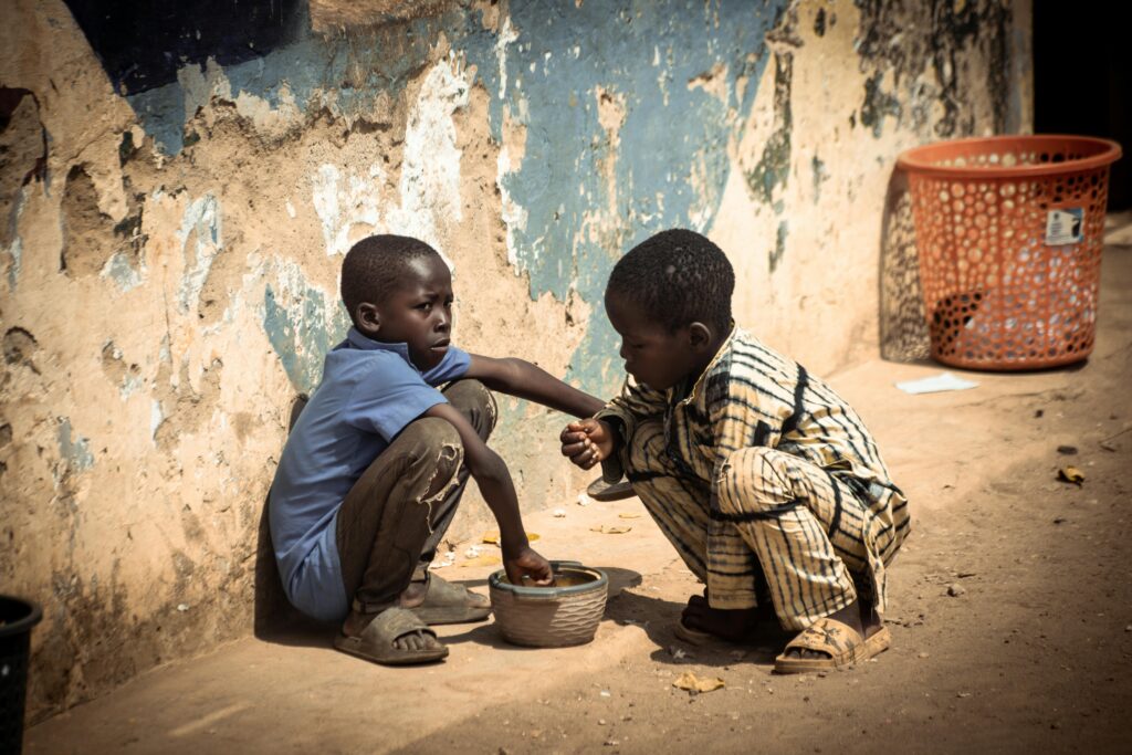 Two boys share a meal outdoors, highlighting themes of poverty and resilience.